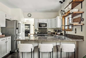 A modern kitchen with stainless steel appliances, a granite countertop, and bar stools.