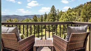Ein Balkon mit Korbmöbeln und einem Tisch, mit Blick auf eine bewaldete Landschaft und Berge in der Ferne.