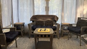Ein gemütliches Zimmer mit Korbmöbeln, darunter eine Couch und Sessel, ein kleiner Tisch mit Fernbedienung und ein hängendes Schild mit der Aufschrift 'Come Gather 'N' Sing Our Porch'.