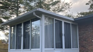 Ein überdachter Patio-Bereich mit weißer Fassade, großen Fenstern und einer Klimaanlage.
