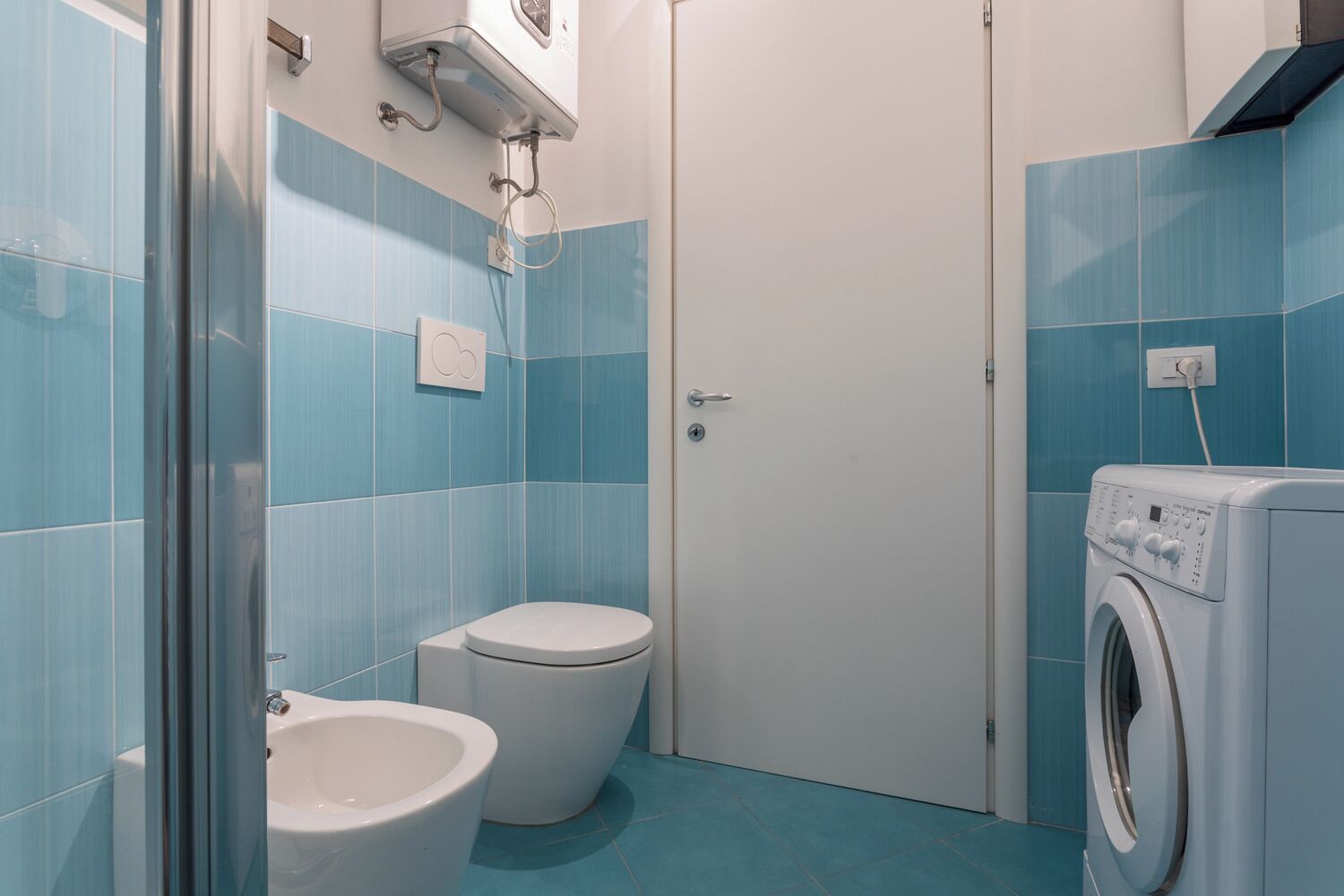 Un baño con azulejos azules, un inodoro blanco, un bidé y una lavadora.
