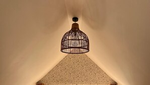 A bedroom with a sloped ceiling, a bed with a textured headboard, a woven light fixture, and a view through a window with curtains. - 2-person cocoon gîte in the heart of nature, very bright, 15 minutes from UTAH BEACH (Picauville)
