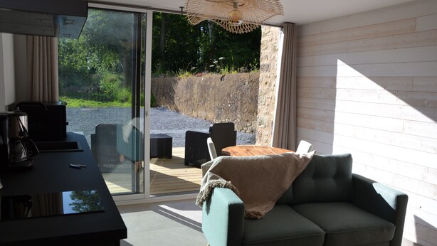 A modern living room with a sofa, a coffee table, and a TV. There is a sliding glass door leading to an outdoor area with a patio table and chairs. - 2-person cocoon gîte in the heart of nature, very bright, 15 minutes from UTAH BEACH (Picauville)