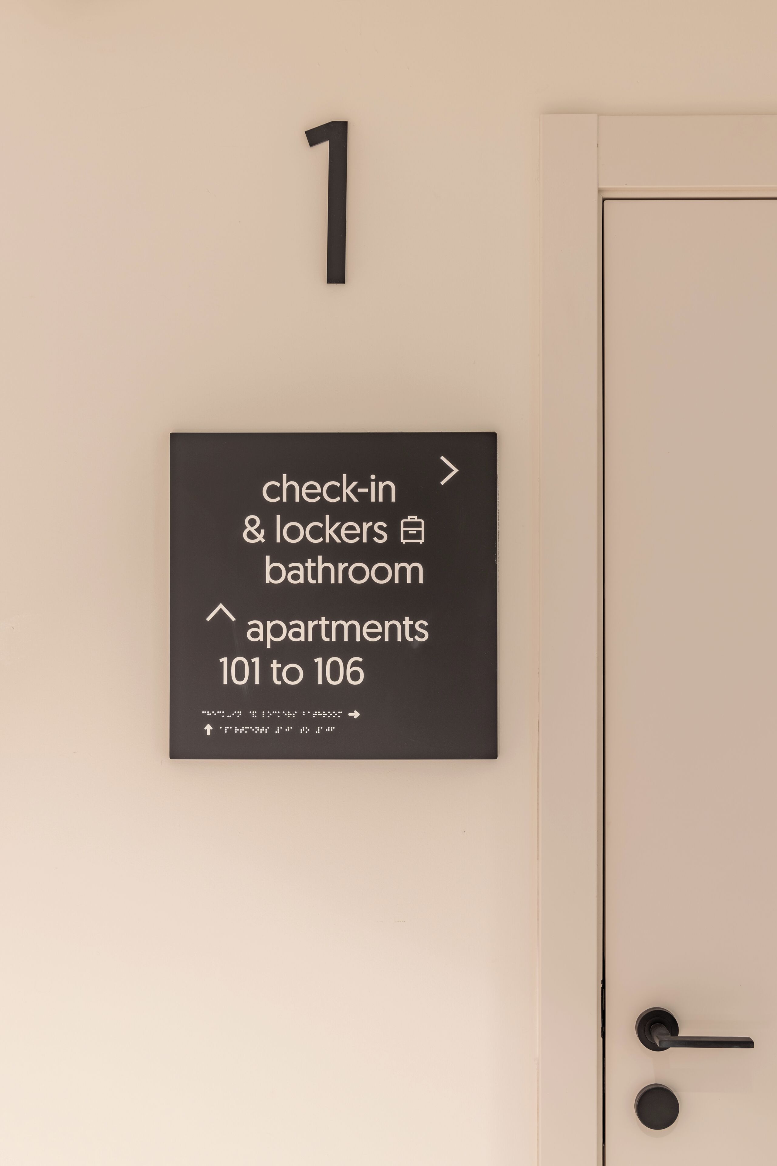 A wall-mounted sign indicating check-in, lockers, bathroom, and apartments 101 to 106.