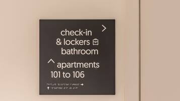 A wall-mounted sign indicating check-in, lockers, bathroom, and apartments 101 to 106.