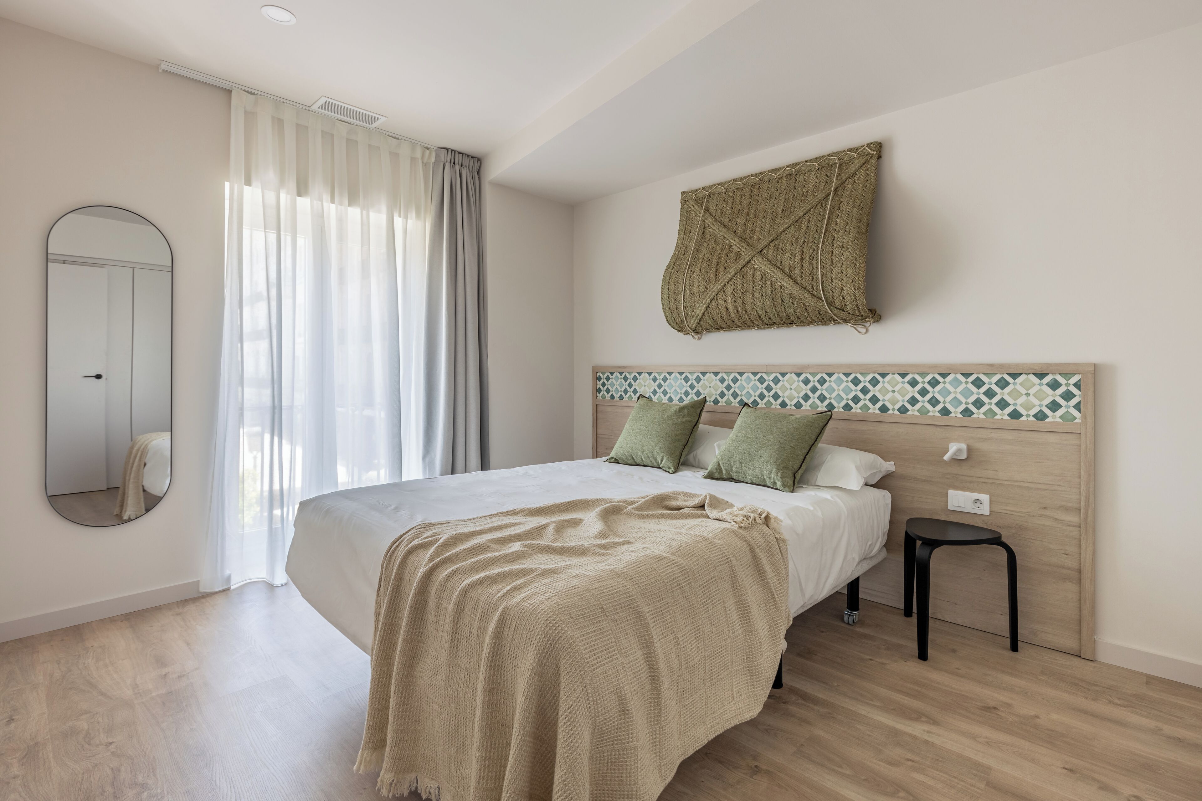 Un dormitorio con una cama, una mesita de noche, un espejo y una ventana con cortinas.