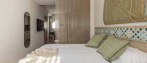 A modern hotel room with a large bed, a wooden headboard, a woven tapestry, and a view of the hallway.