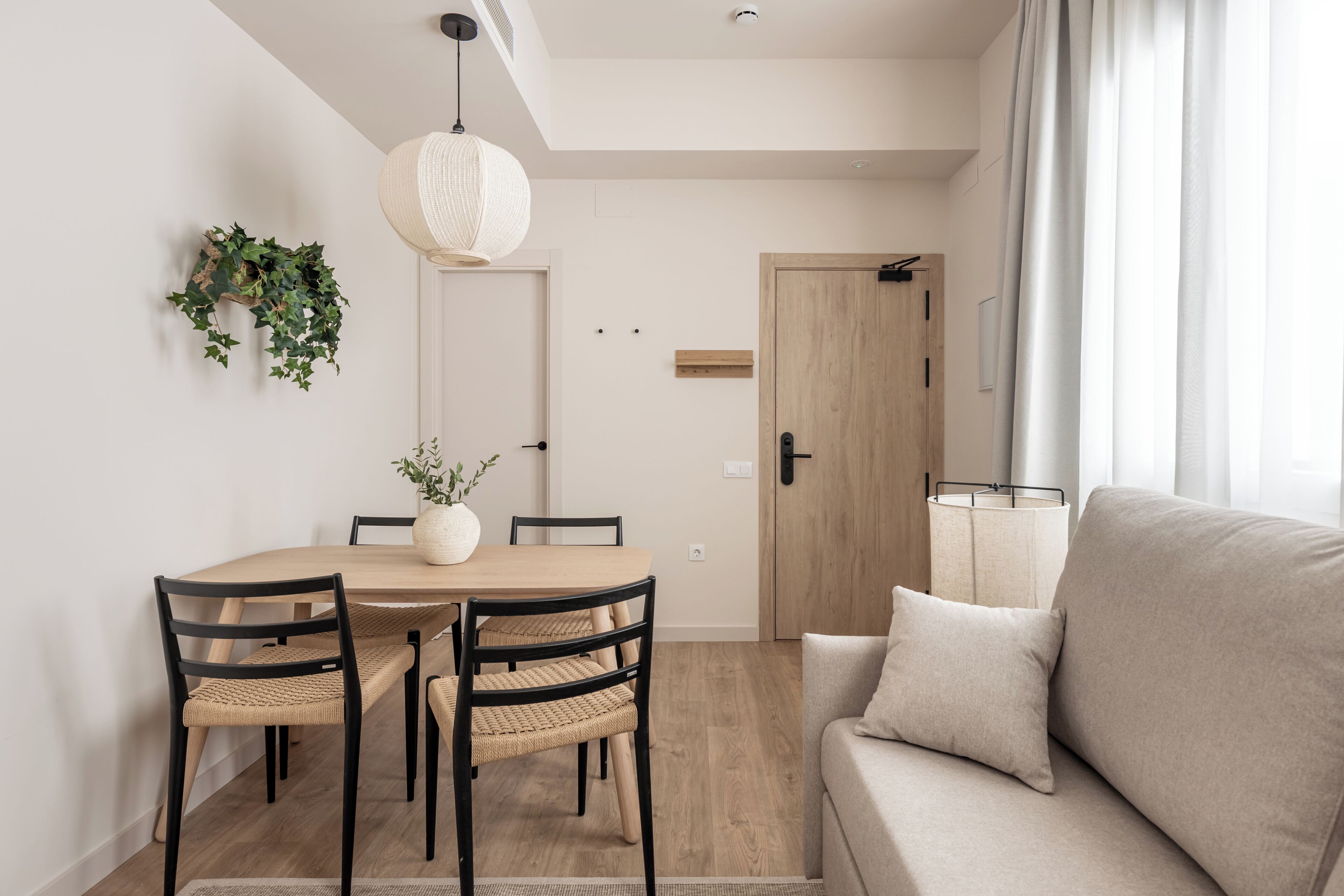 Un salon moderne avec une table à manger en bois, deux chaises, un canapé et un luminaire suspendu.