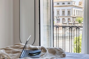 En bærbar computer på en seng med udsigt til en balkon og bygninger.