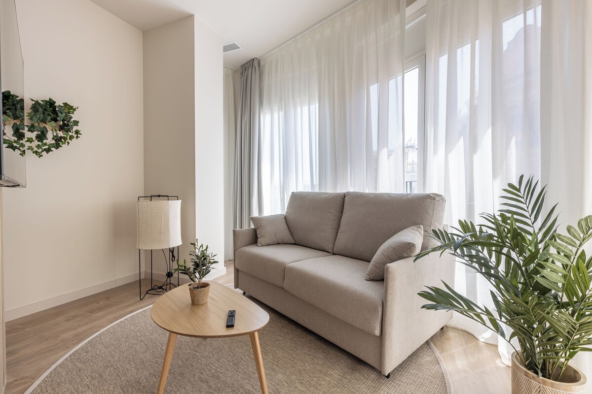 Un soggiorno moderno con un divano color beige, un tavolino rotondo in legno e una pianta in vaso.