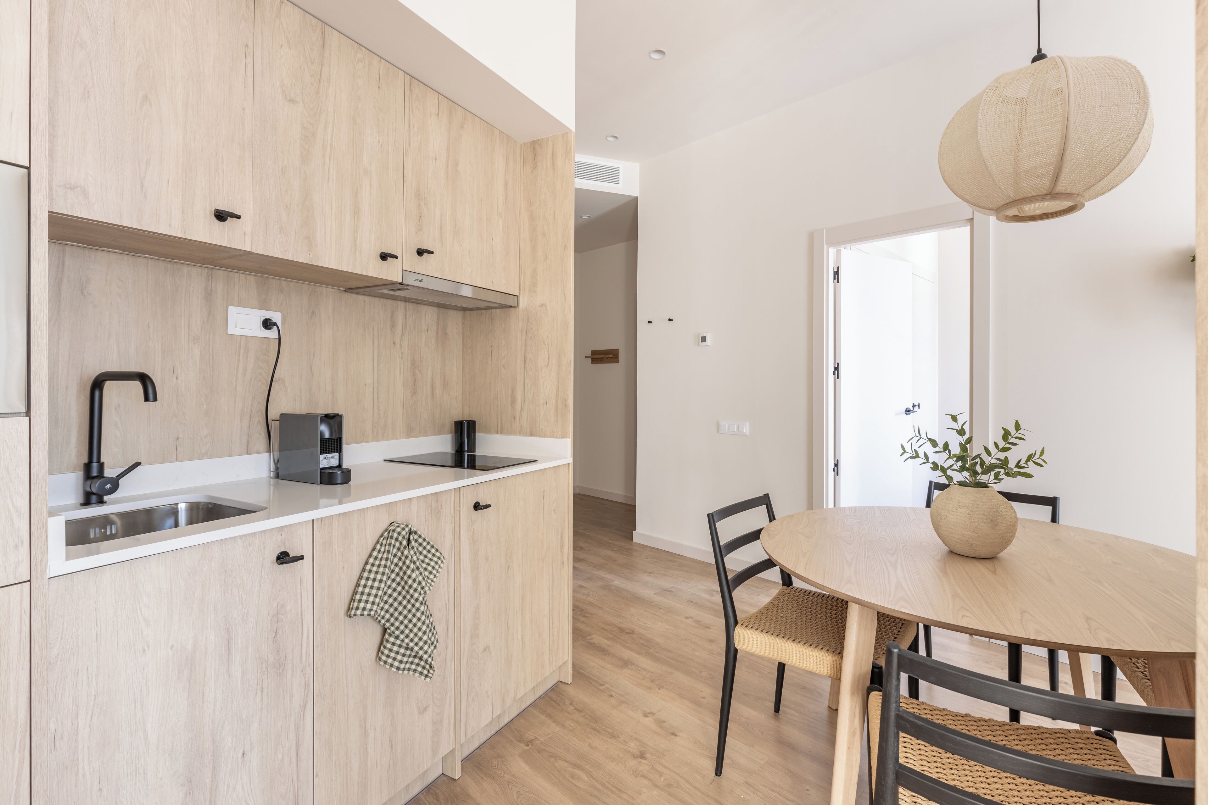 A modern kitchen with wooden cabinets, a built-in stove, and a dining area with a round table and chairs.