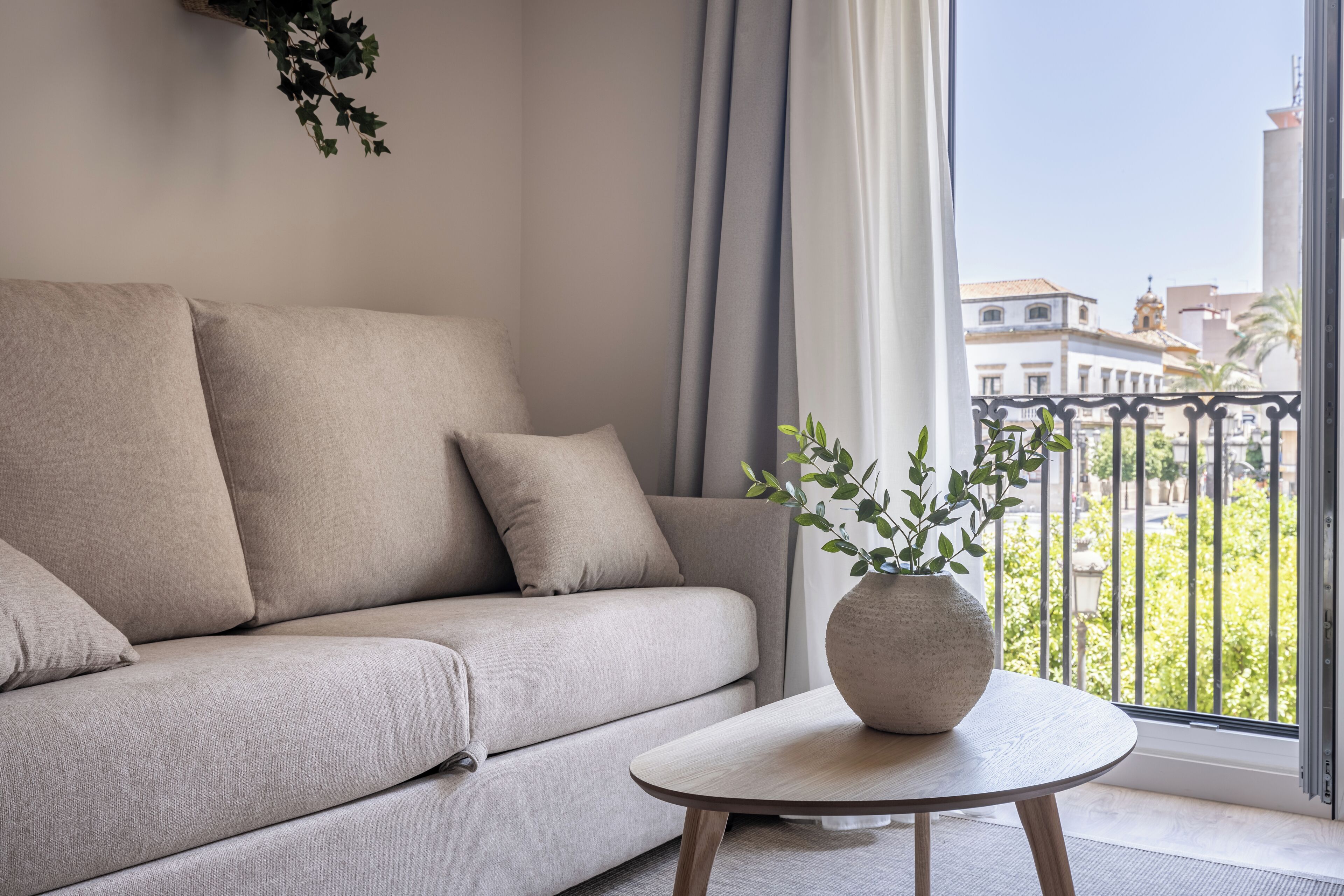 Een moderne woonkamer met een beige bank, een ronde houten salontafel en een potplant.