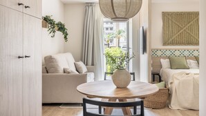 Een moderne woonkamer met een ronde houten tafel, een bank, een bed en een grote geweven lamp.
