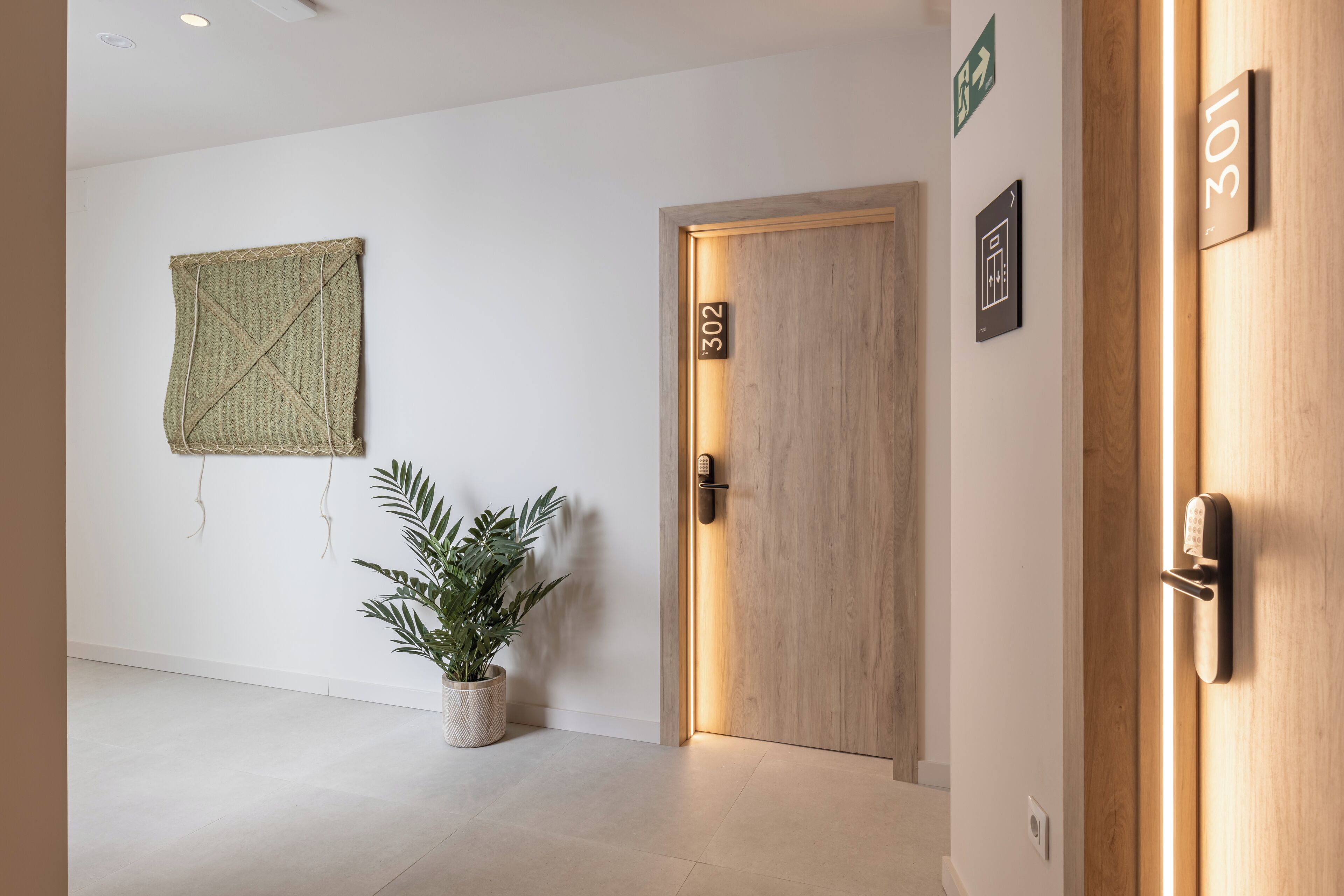 A hallway with a wooden door labeled "302", a potted plant, and a wall-mounted sign with a symbol.