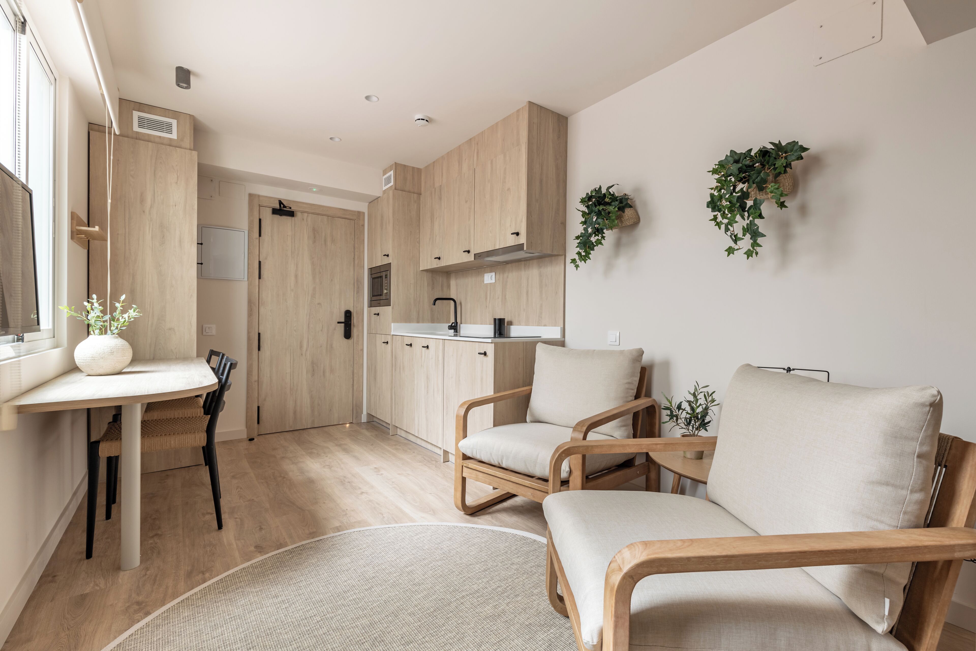 A modern kitchen with wooden cabinets, a dining area with a table and chairs, and two cushioned chairs in the living area.
