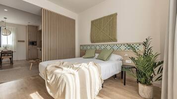 Ein modernes Schlafzimmer mit einem großen Bett, Holzboden, einer Küchenzeile und einem Blumentopf.