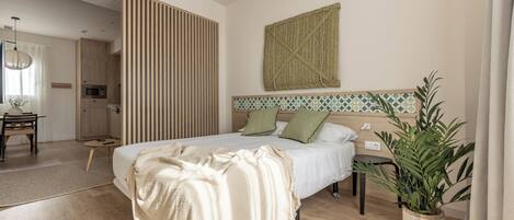 A modern bedroom with a large bed, a wooden floor, a kitchen area, and a potted plant.