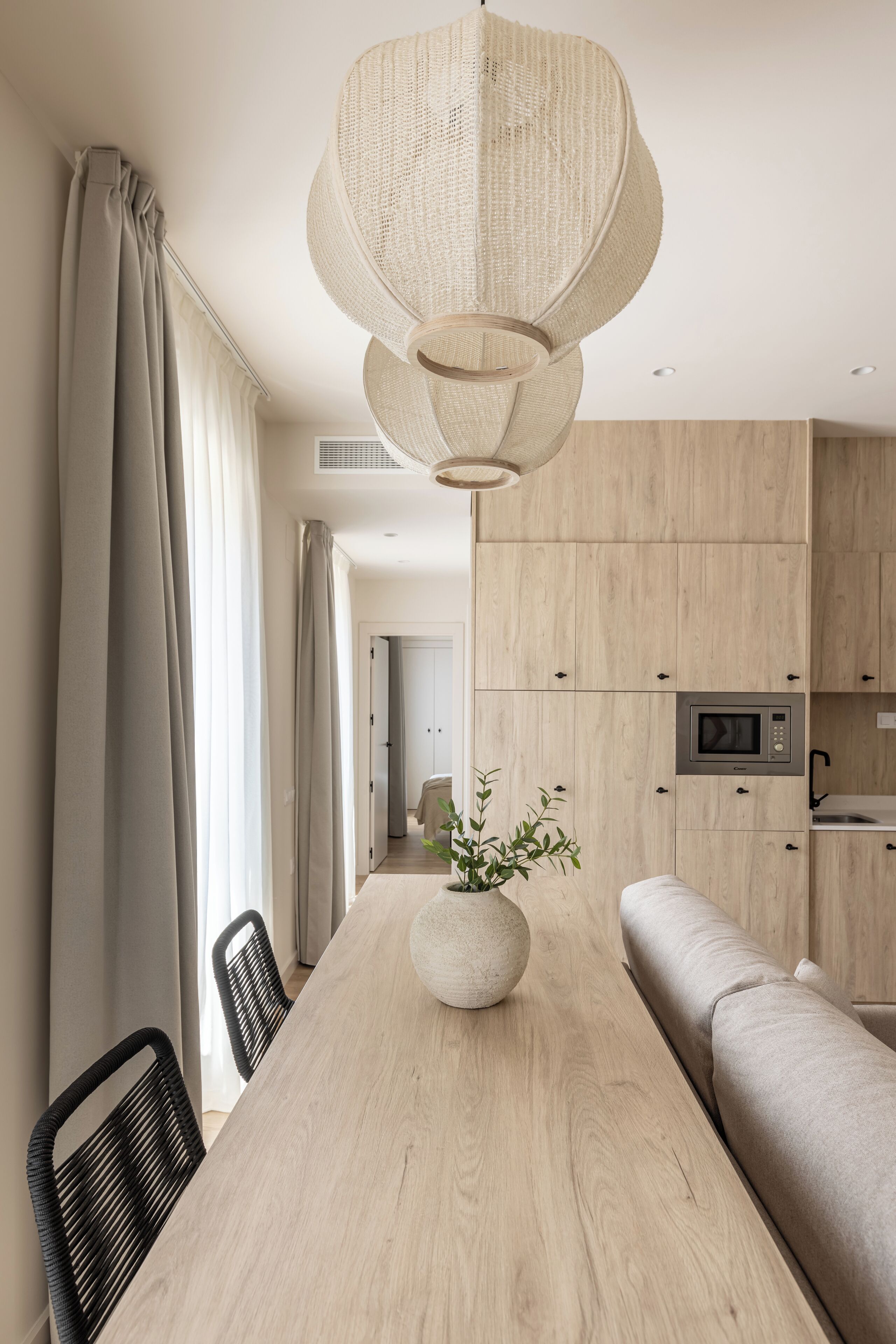 Een moderne keuken met houten kastjes, een inbouwmagnetron en een eethoek met een houten tafel en stoelen.