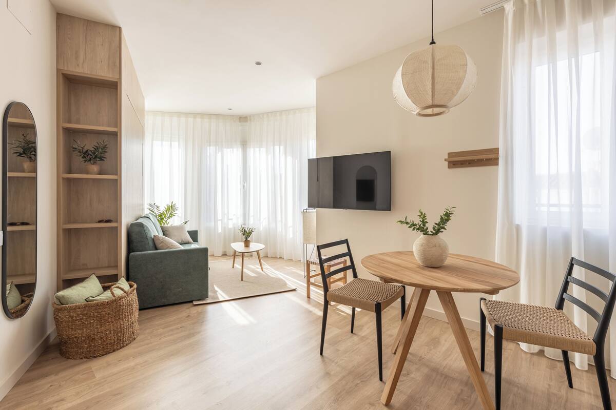 Un salon moderne comprenant un canapé, une table à manger avec des chaises, un téléviseur fixé au mur et un grand miroir.