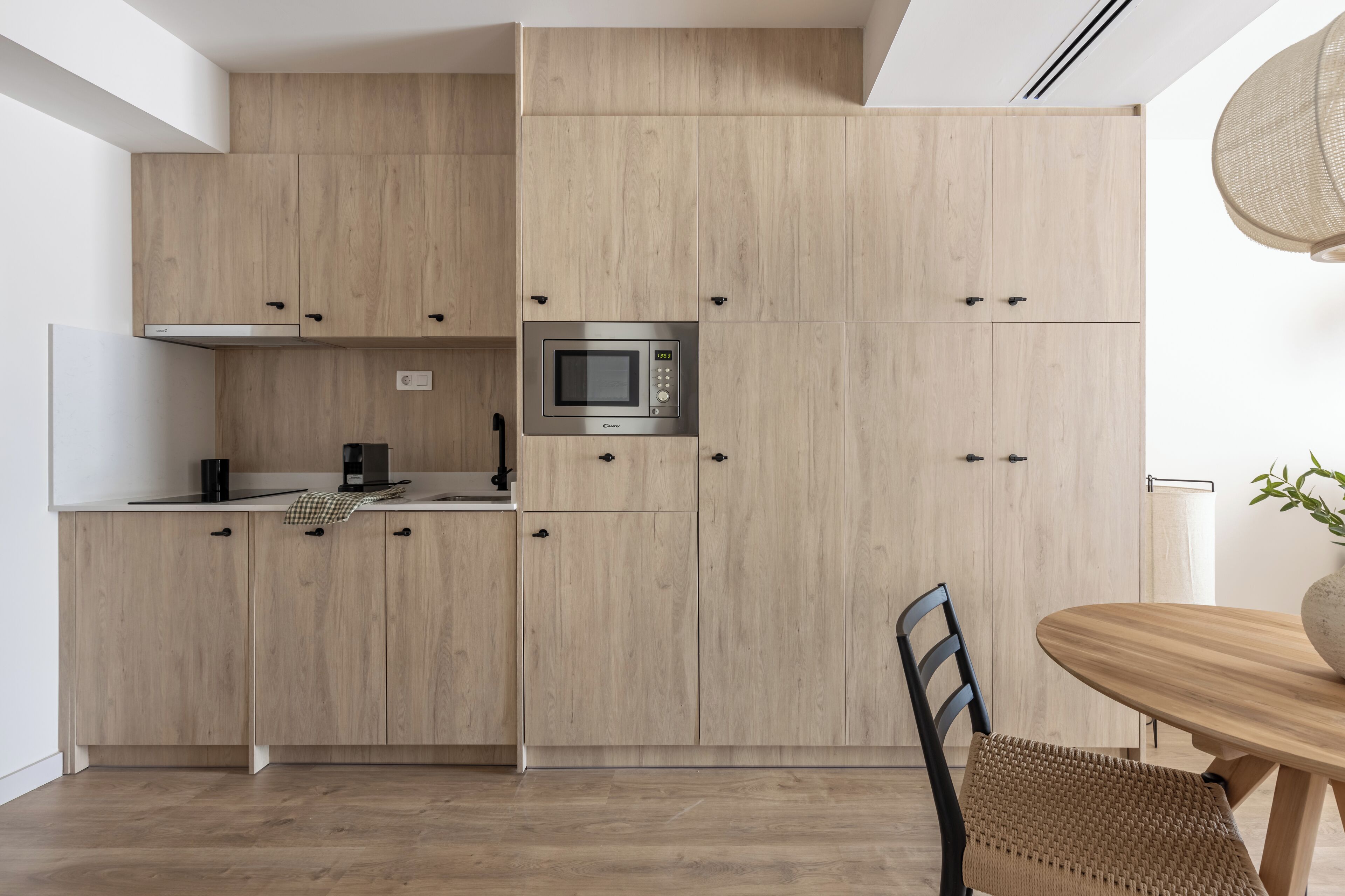 Een moderne keuken met houten kastjes, een magnetron en een eethoek met een houten tafel en stoel.