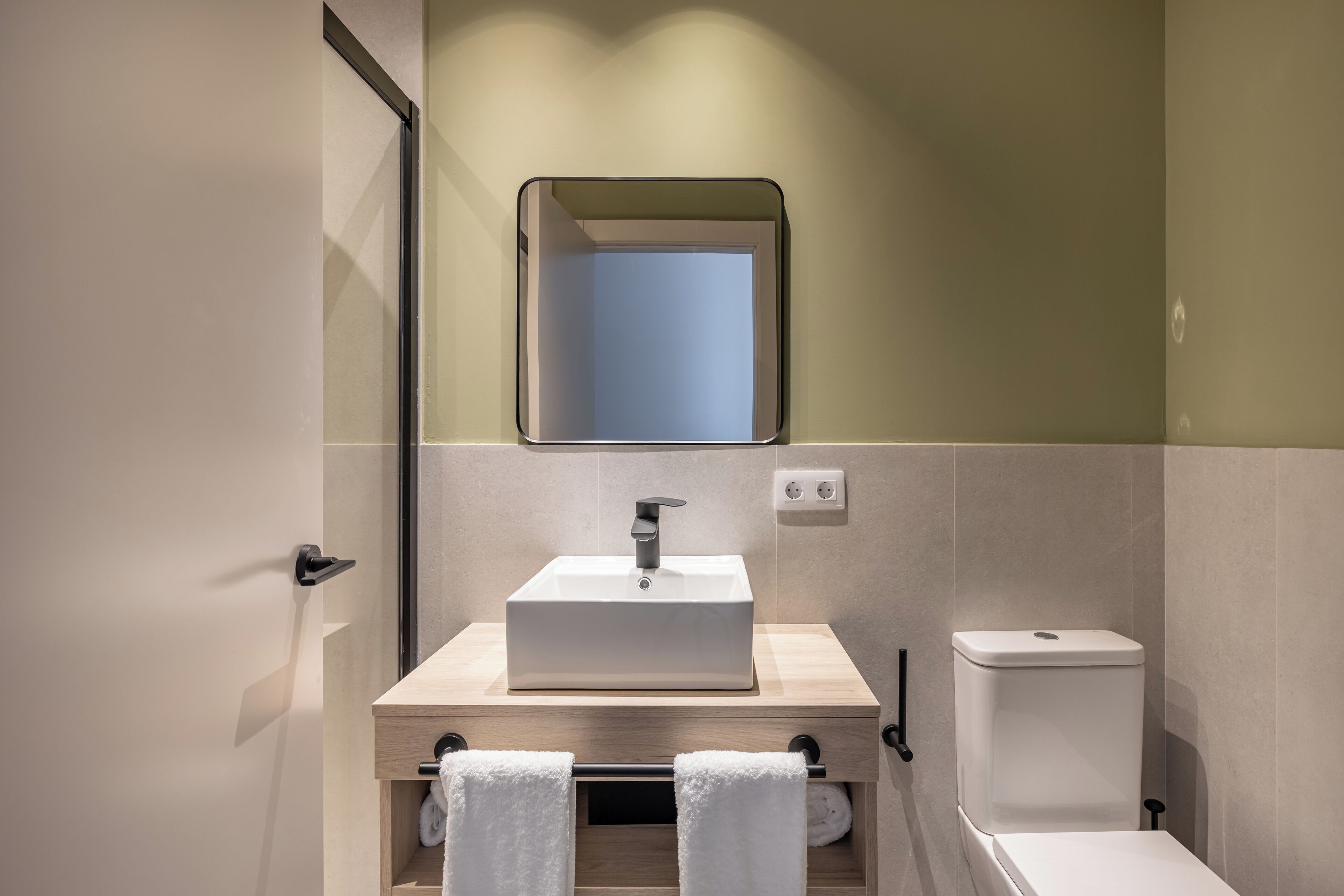 A modern bathroom with a rectangular sink, a mirror above it, and a toilet to the right.