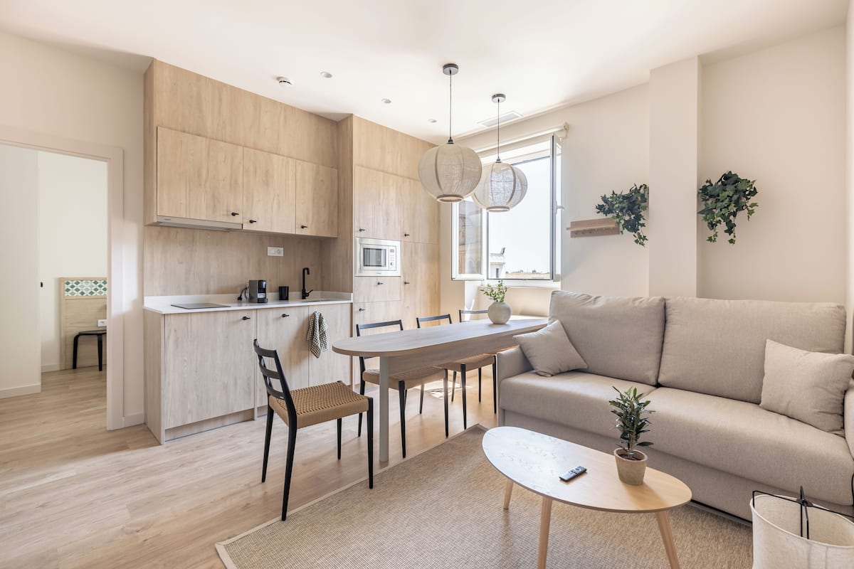 Une cuisine moderne avec des meubles en bois, une table à manger et des chaises. On y trouve également un canapé et une petite table sur laquelle est posée une plante.