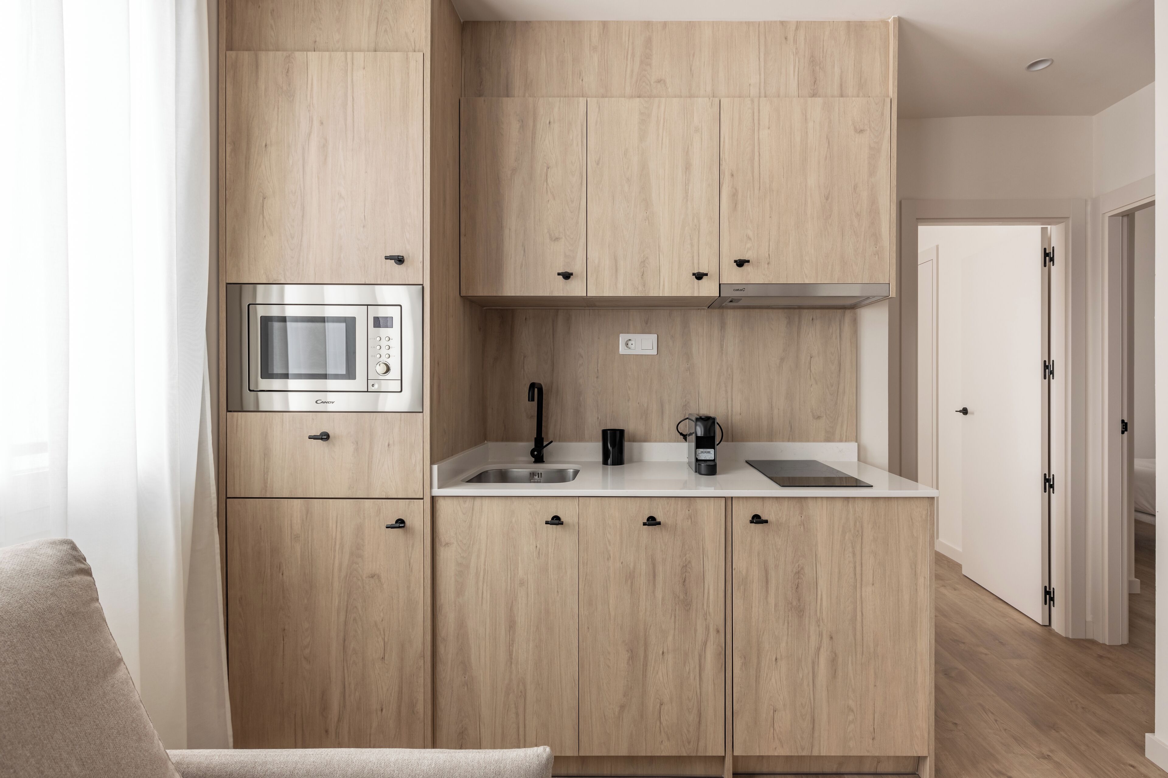 A modern kitchen with wooden cabinets, a built-in microwave, a coffee maker, and a sink.