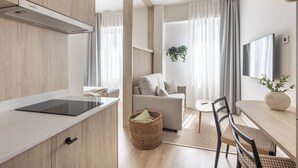 Een moderne keuken met een inbouwfornuis, een eethoek met een tafel en stoelen, en een zithoek met een bank en gordijnen.