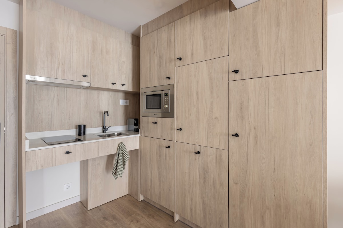 A modern kitchen with light wood cabinetry, a stainless steel microwave, and a white countertop.