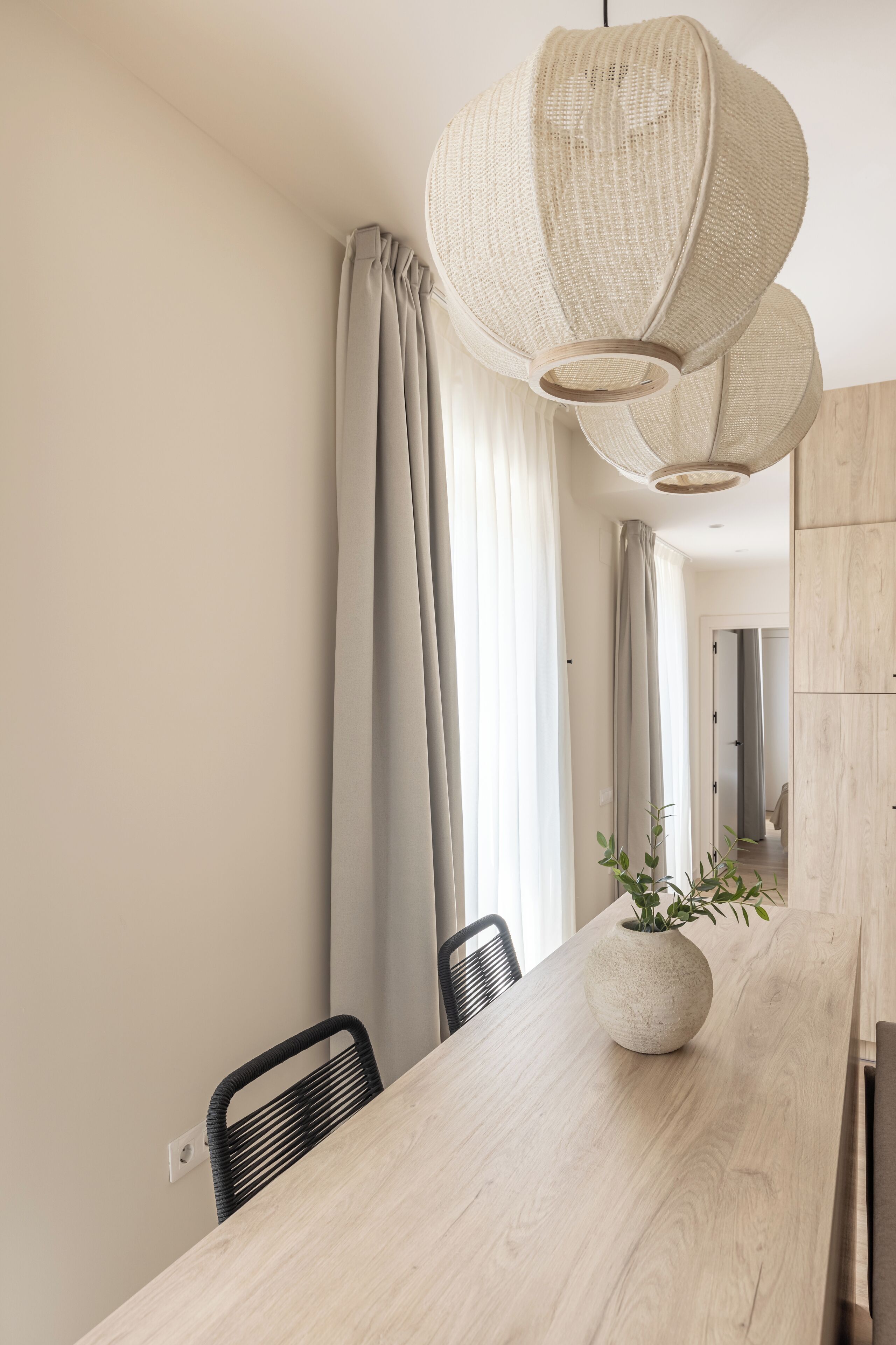 Un espace repas moderne avec une table en bois, des chaises noires et un luminaire suspendu en fibres tressées.