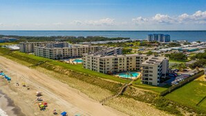 A beachfront hotel with multiple buildings, a swimming pool, and a beach area with umbrellas. - Summer Winds 436B- 2BR Condo w/ Ocean Views & Pools! (Indian Beach)