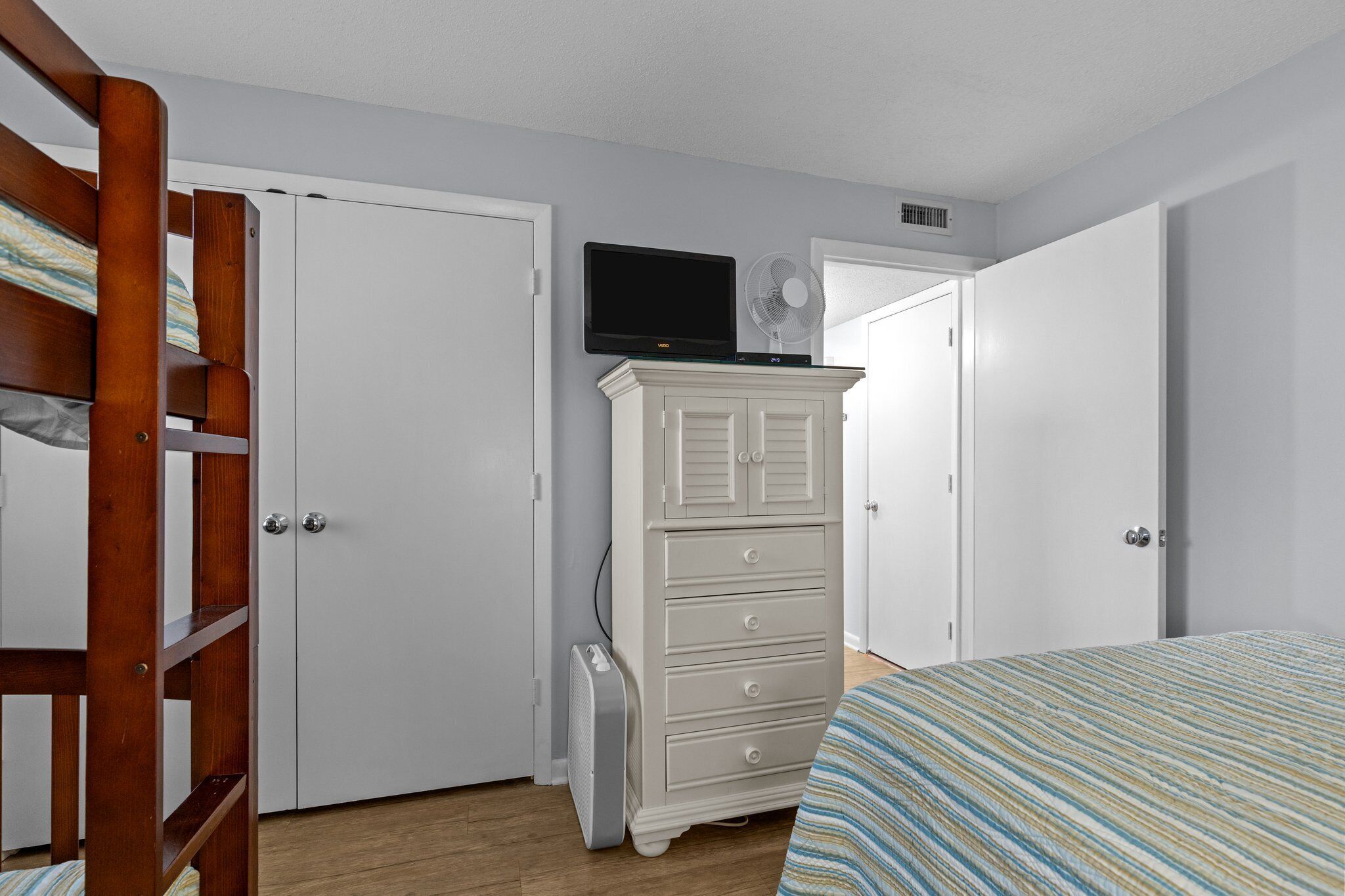 A bedroom with a bunk bed, a dresser, a television, and a fan.