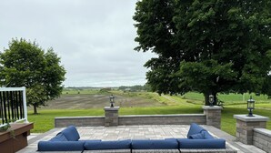 A patio with a wicker sofa, stone pillars, and a view of a field.