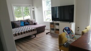 A living room with a sofa, a TV, a dining table, and a chair.