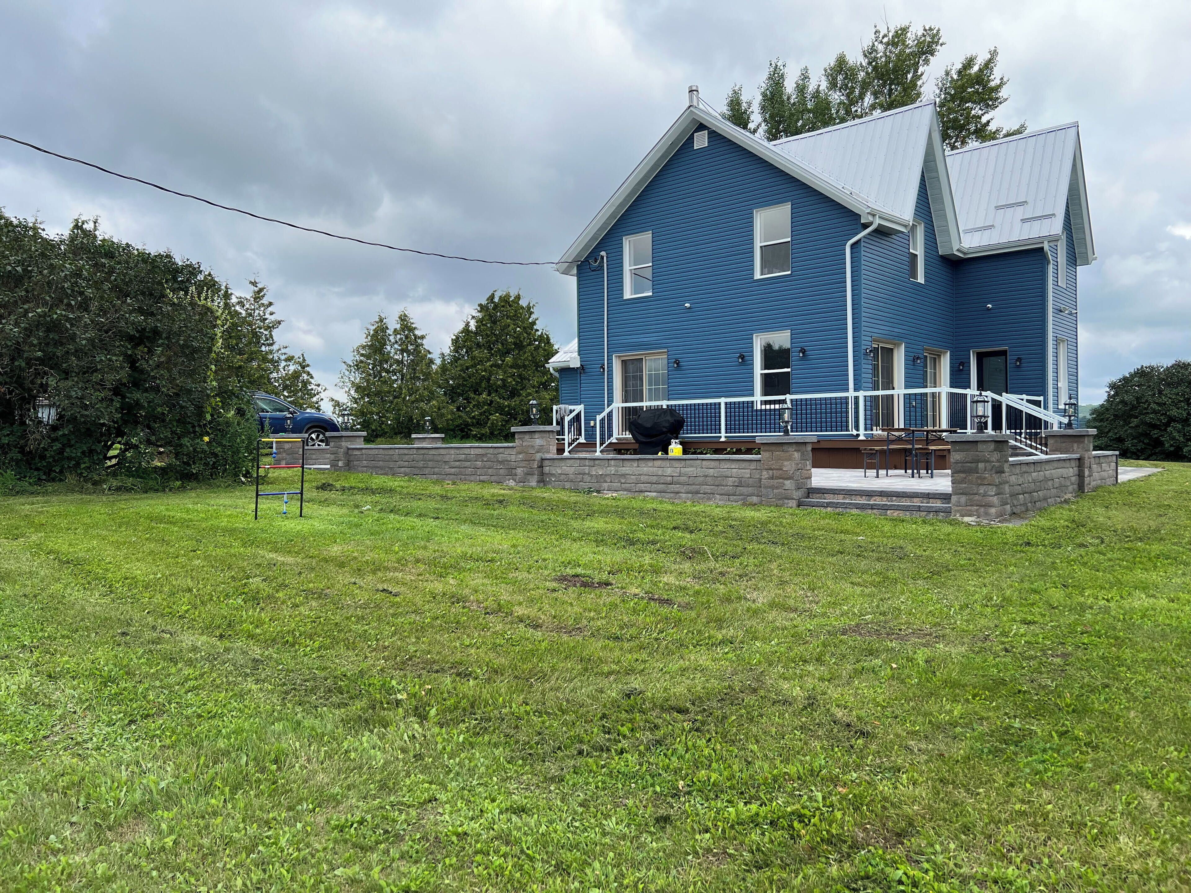 A two-story blue house with a front porch, a stone retaining wall, and a grassy yard.
