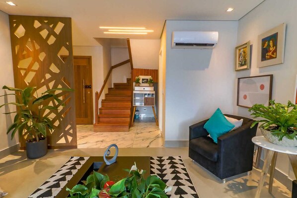 Un salon moderne avec un escalier, un canapé noir agrémenté d’un coussin turquoise et une plante en pot.