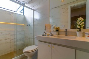 A modern bathroom with a glass shower enclosure, a white toilet, a marble vanity with a mirror, and a potted plant.