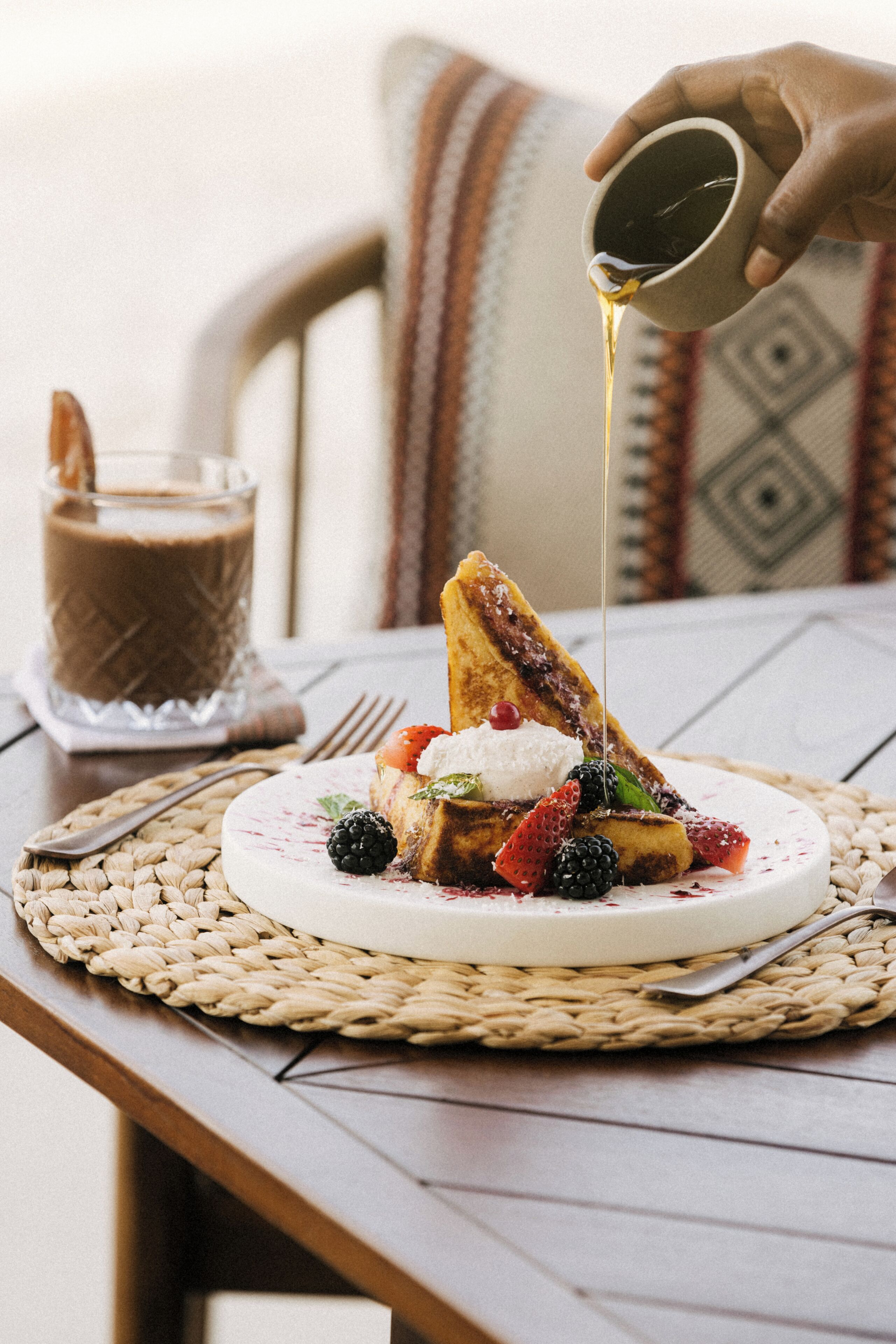 Un plato de desayuno con tostadas, bayas, crema batida y una taza de café.
