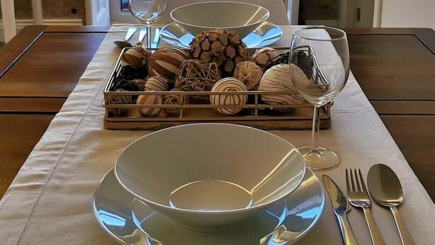 A dining table set with a bowl, wine glasses, and cutlery, with a scenic view through a balcony door. - Solar dos Condes da Azenha (Sernancelhe)