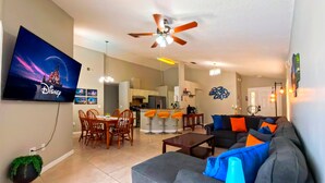 A living room with a gray sofa, orange bar stools, a dining table, and a TV displaying the Disney logo. - Private Pool • Game Room • Near Disney (Davenport)