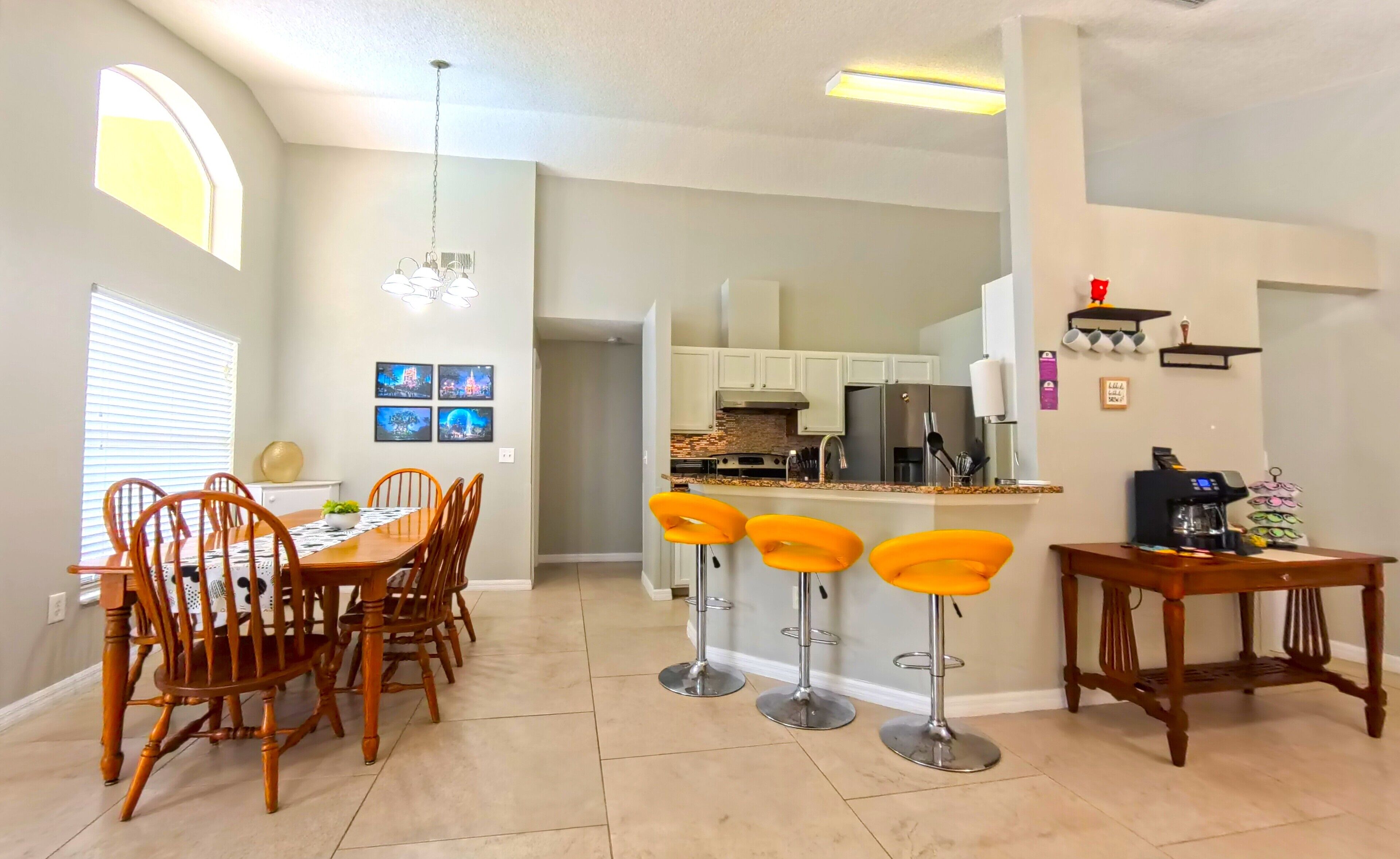 A modern kitchen with a dining area, featuring a central island with bar stools, a chandelier, and a refrigerator.