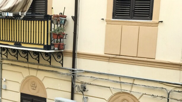 Une façade d’immeuble avec un balcon, une composition florale et un coffret de raccordement électrique.