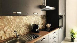 Une cuisine moderne équipée d’un évier en acier inoxydable, d’une machine à café et d’une bouilloire posées sur le plan de travail.