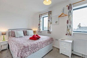 A bedroom with a bed, bedside tables, a radiator, and a window with curtains.