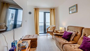 A living room with a sofa, ottoman, chair, and a flat-screen TV. - 3 Bed in Ilfracombe (oc-s29585) (Ilfracombe)