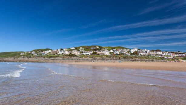 A coastal beach with clear skies, a sandy shore, and a row of houses on a hillside. - 3 Bed in Ilfracombe (oc-s29585) (Ilfracombe)