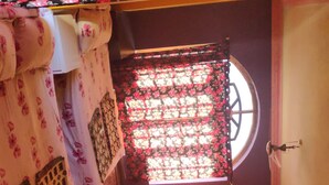 Ein gemütlicher Raum mit Fenster, einem Bett mit floralem Bettbezug, einem kleinen Tisch und einem Sessel.