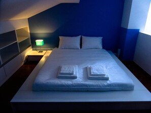 A neatly made bed with folded towels, a bedside lamp, and a headboard. - Guesthouse Ponta Delgada (Ponta Delgada)