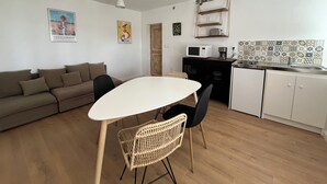 Ein kompakter Wohnbereich mit Küchenzeile, einem Essbereich mit weißem Tisch und Stühlen, einem braunen Sofa und einer kleinen Küchenarbeitsplatte.