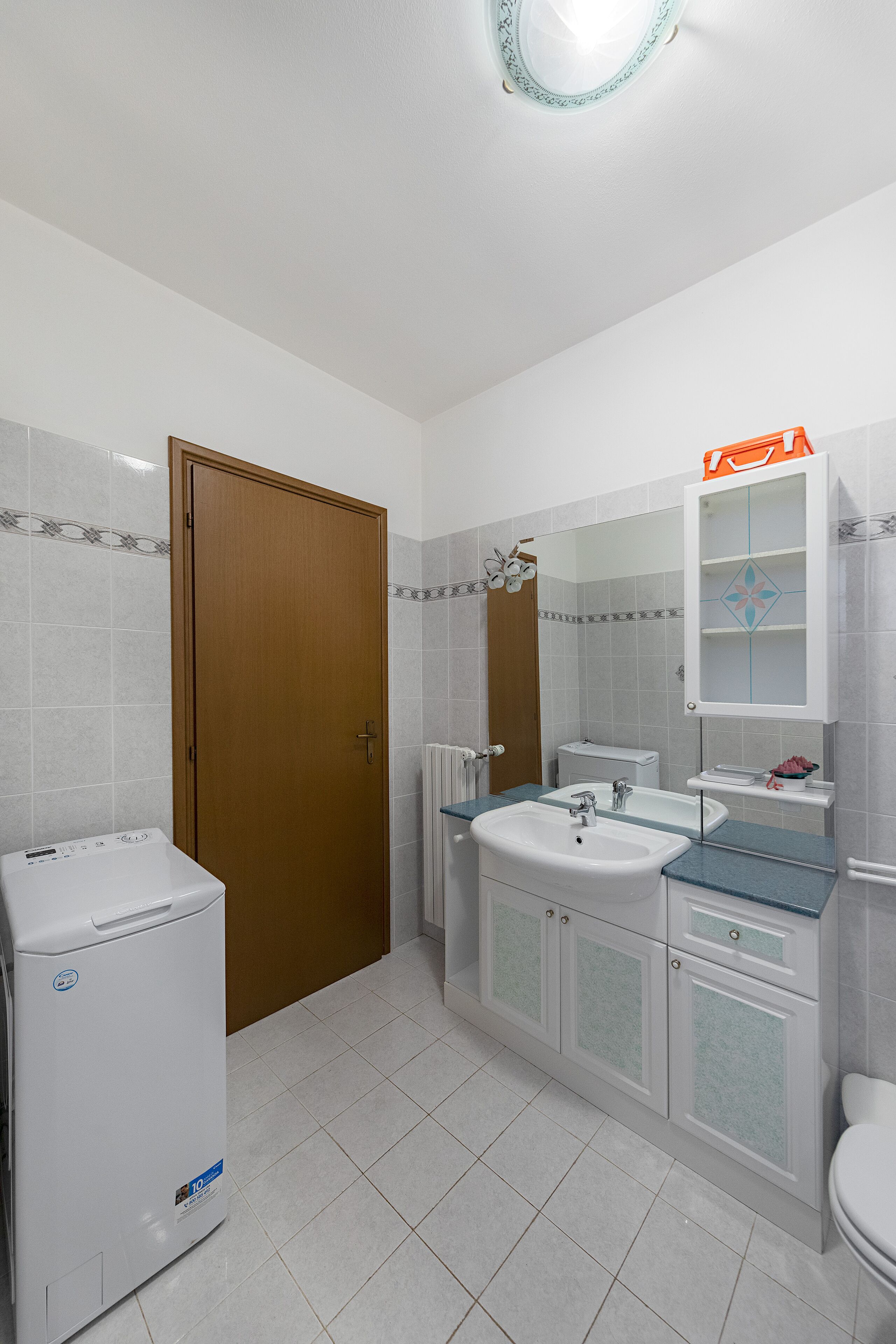 Ein Badezimmer mit Holztür, Waschbecken in Weiß, Spiegel und Toilette in Weiß.
